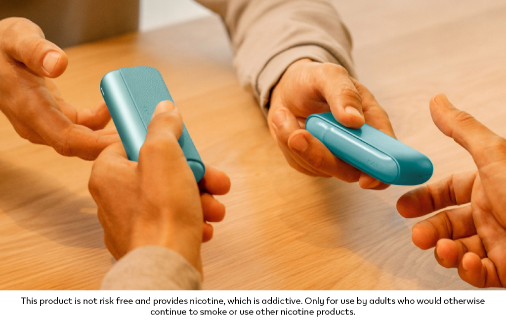 Two hands exchanging a Breeze Blue IQOS ILUMA i PRIME device with a Breeze Blue IQOS ILUMA i device