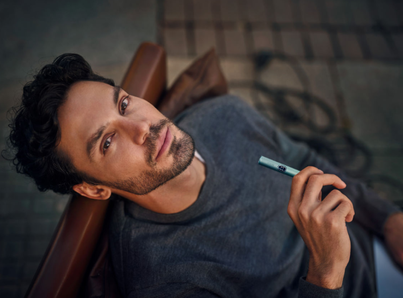 Man sitting on a bench is holding an IQOS ILUMA i holder