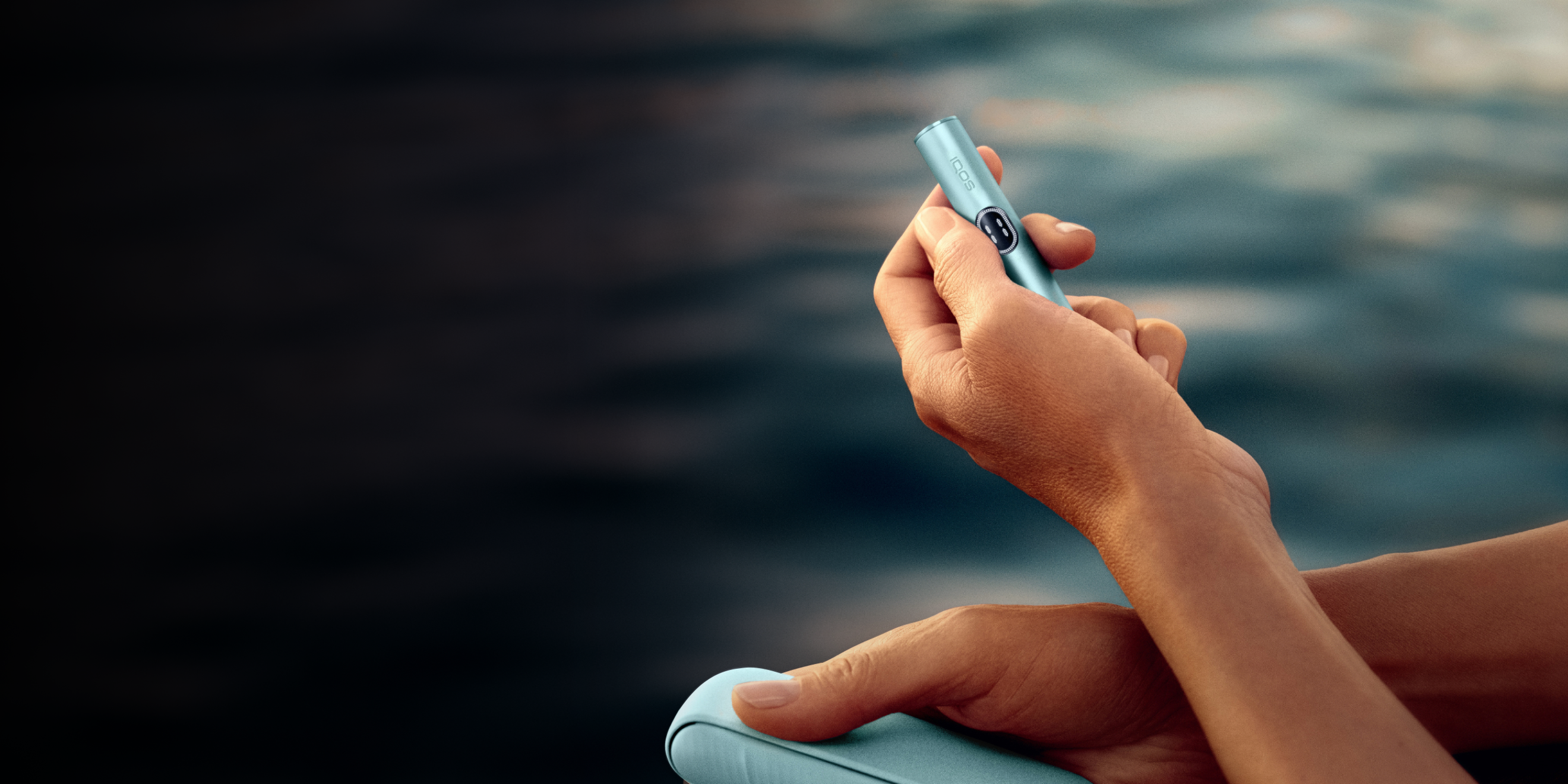 A person holding an IQOS ILUMA i Holder in Breeze Blue color, above the sea