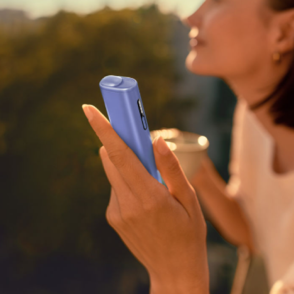 A smiling woman with an IQOS ILUMA device.