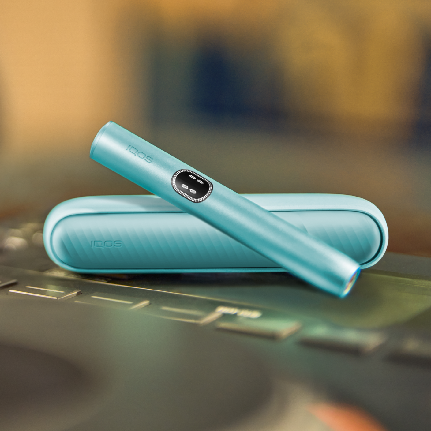Βάση IQOS ILUMA i PRIME και ο φορτιστής της σε χρώμα Breeze Blue πάνω σε μια κονσόλα DJ.