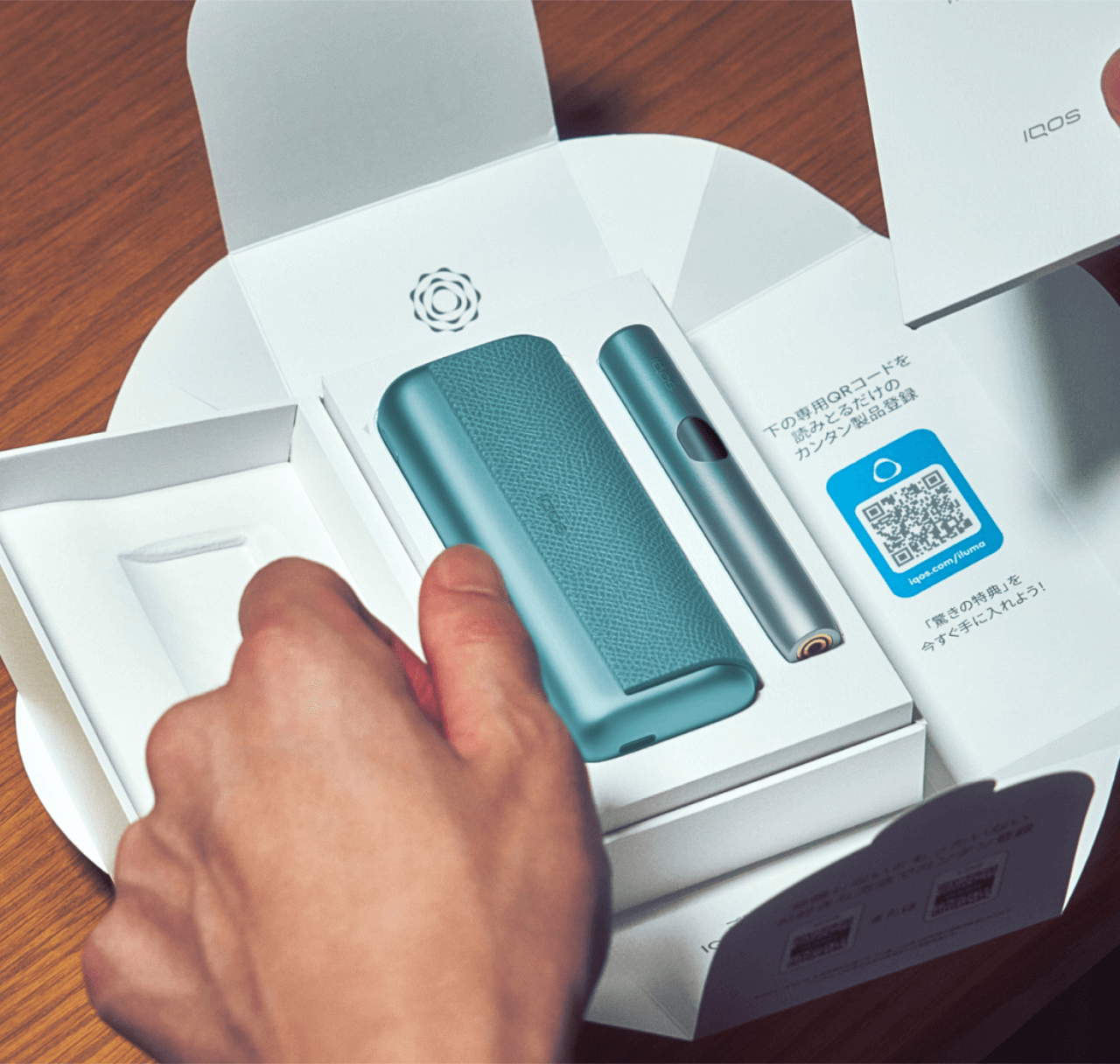 Man opening an IQOS box on a table revealing an IQOS ILUMA i device.