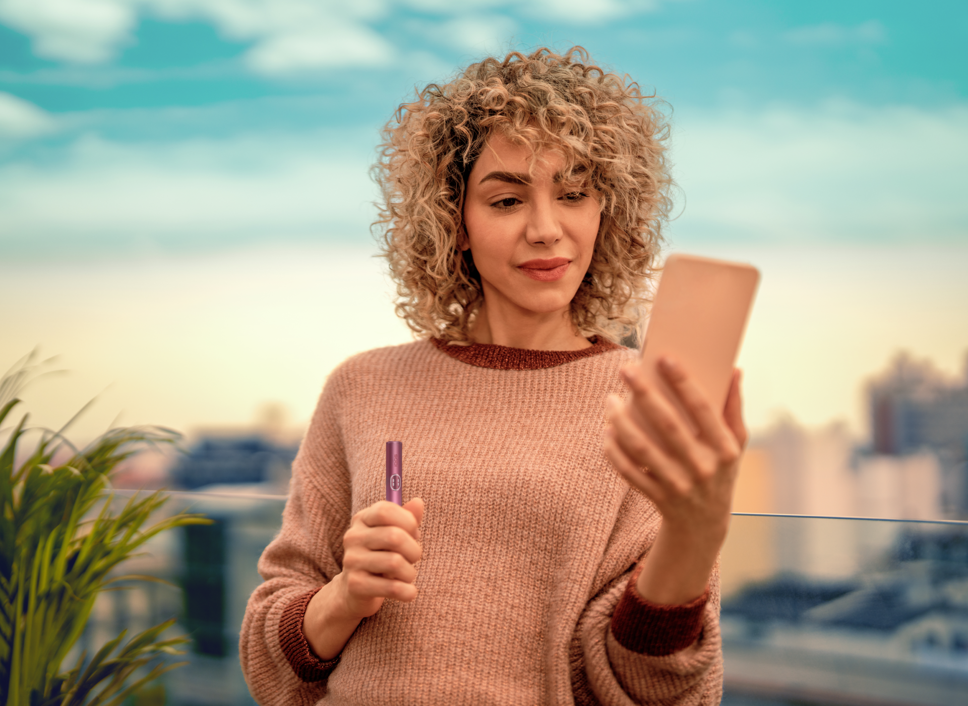 A woman is holding a smartphone and an IQOS ILUMA i holder is color Garnet Red.
