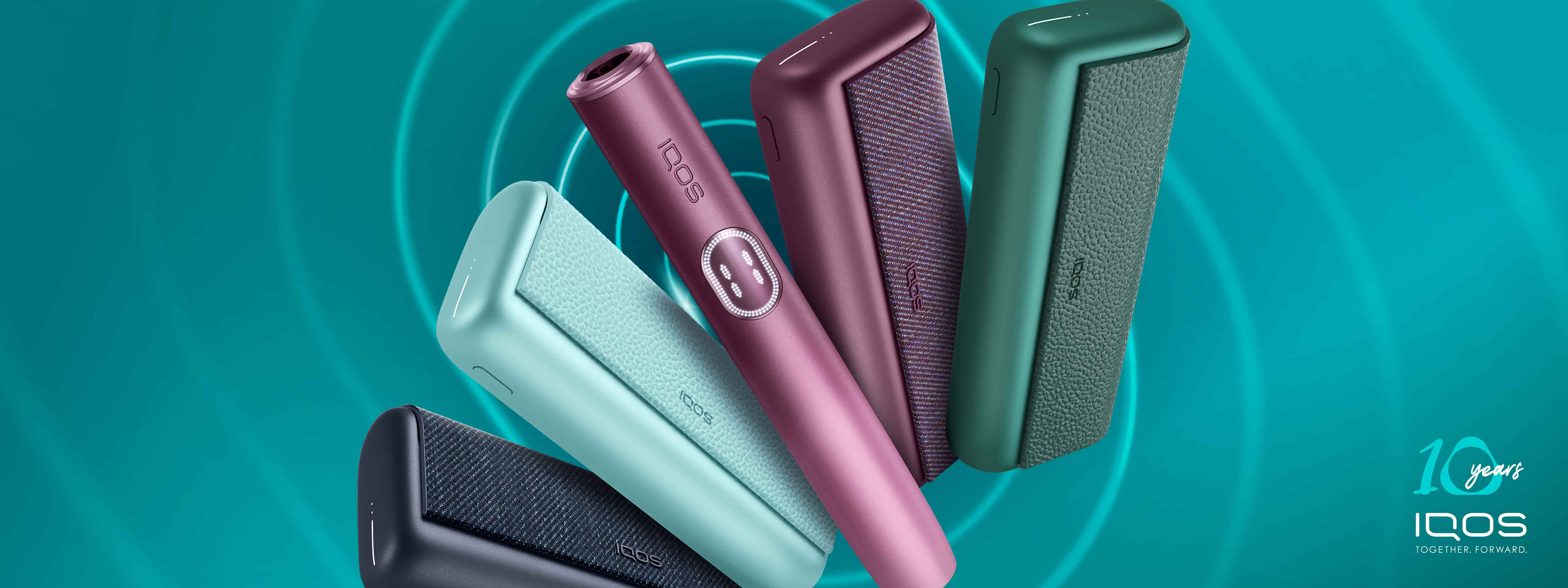 Four  IQOS ILUMA i PRIME devices - black, blue, red and green - on a dark turquoise  background