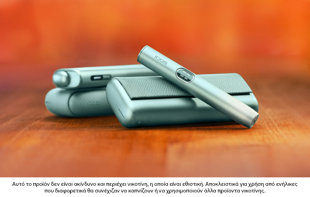 Πράσινη συσκευή IQOS ILUMA i PRIME πάνω από τον φορτιστή της, με μια συσκευή IQOS ILUMA στο φόντο.