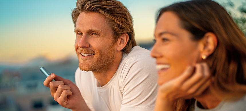 A man holding and IQOS ILUMA and a woman looking at the sunset