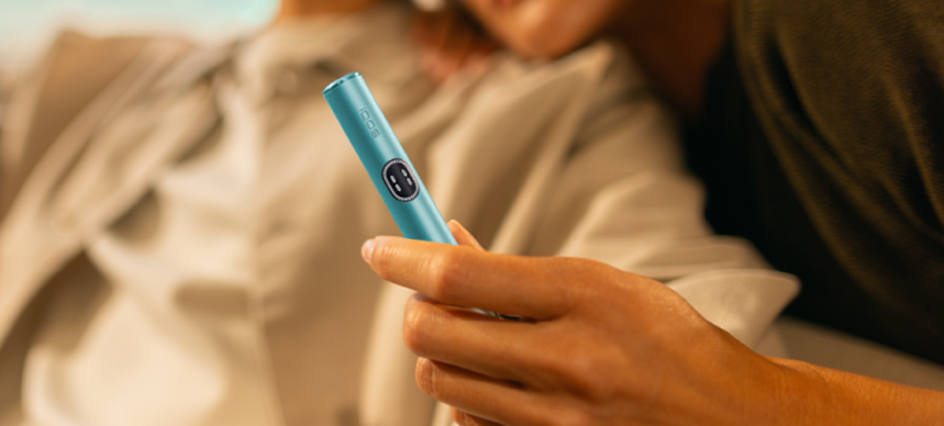 A couple hugging and the woman holds a Breeze Blue IQOS ILUMA i device.