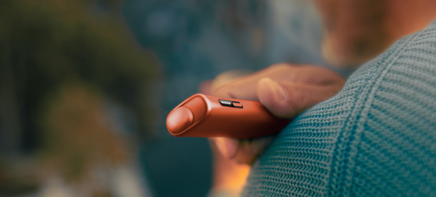 Male hand holding a Terracotta IQOS ILUMA i ONE device.