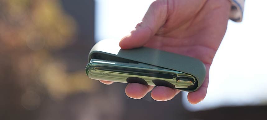 woman looking outside of a car window holding an IQOS 3 DUO