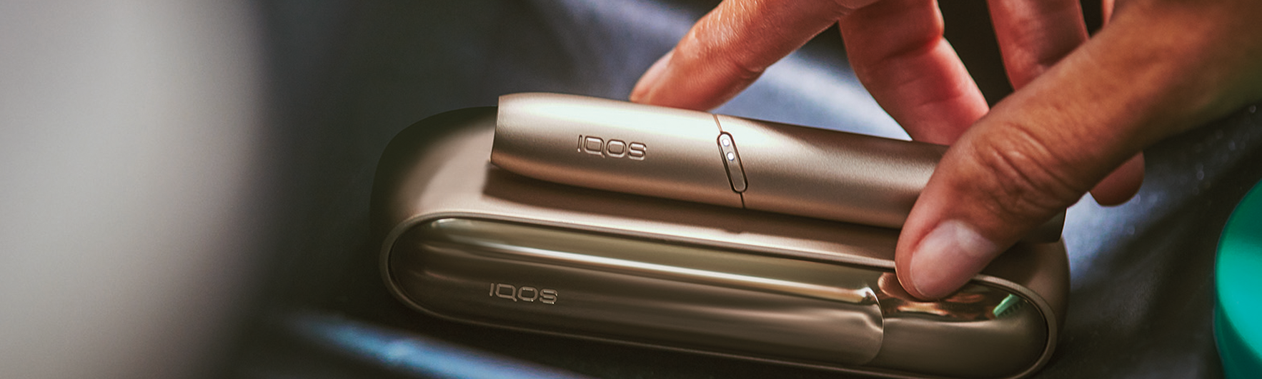 hand placing IQOS 3 DUO Gold on leather surface