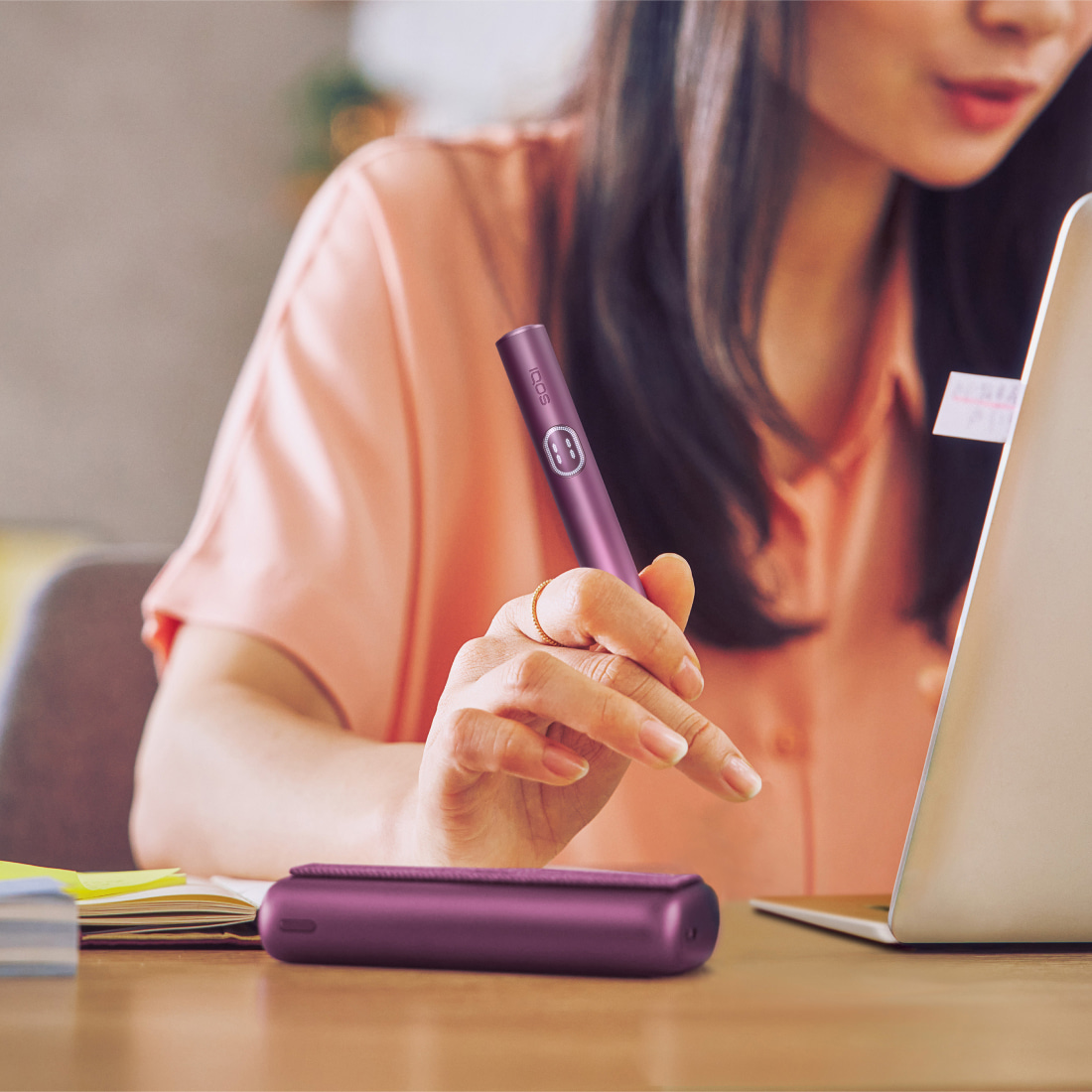 Person working on a laptop and holding a garnet red IQOS ILUMA i PRIME device