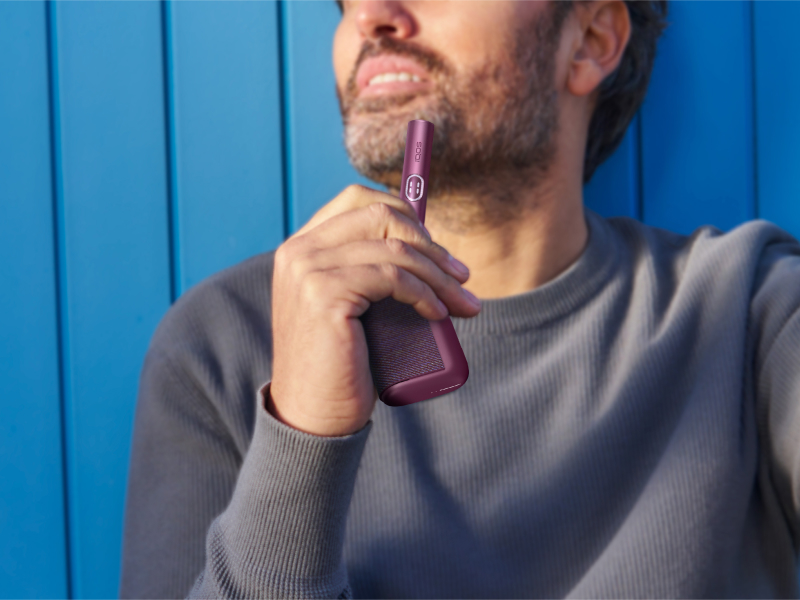 Man holding a garnet red IQOS ILUMA i PRIME device and its charger