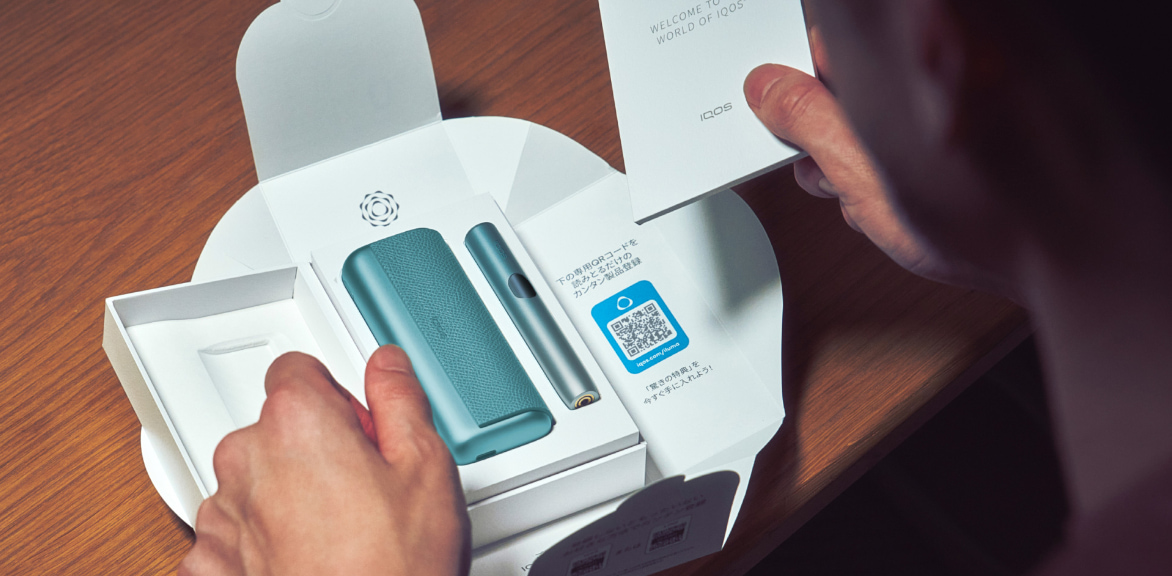 Detail of hands unboxing a blue IQOS ILUMA i PRIME device