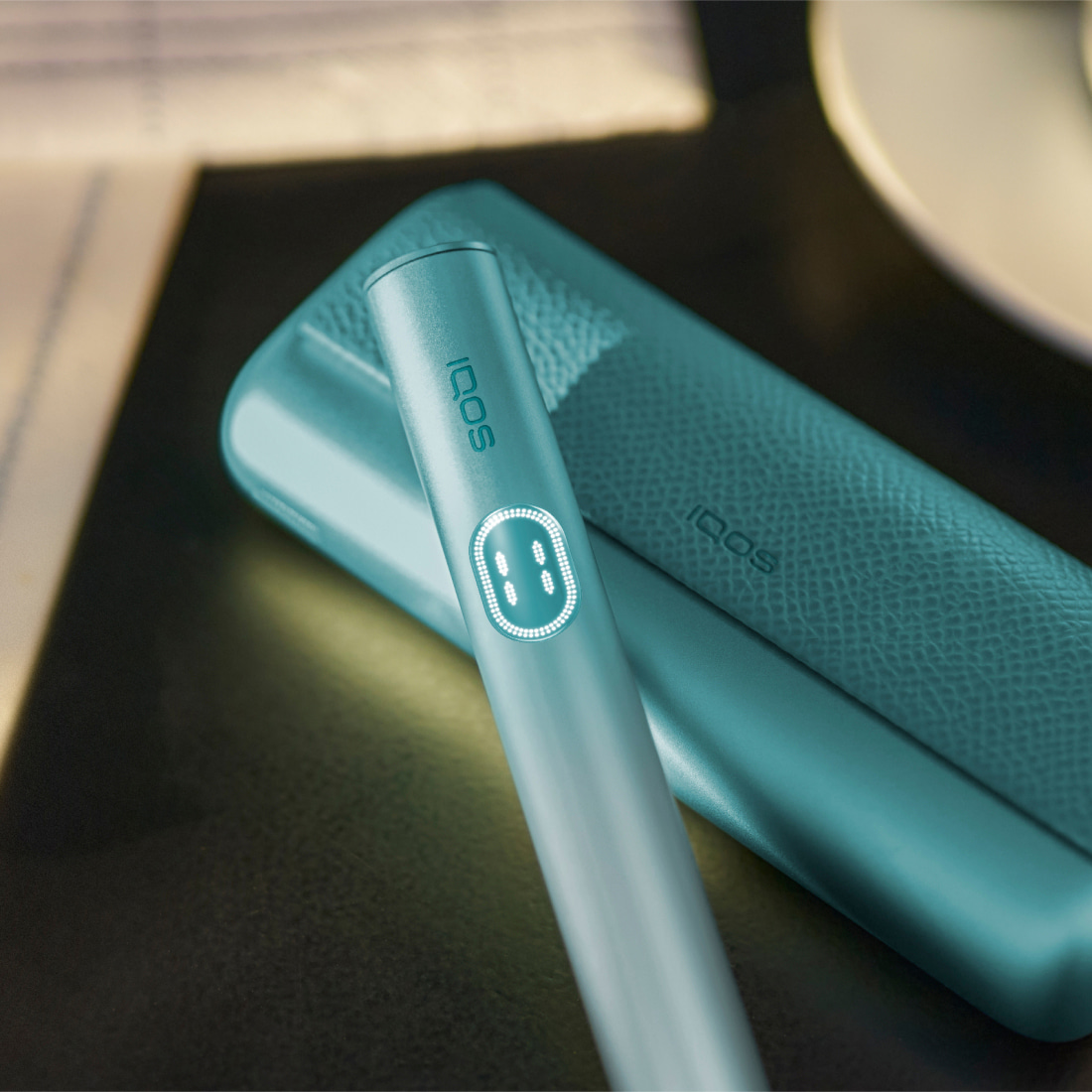 Blue IQOS ILUMA i PRIME device and its charger on a green table