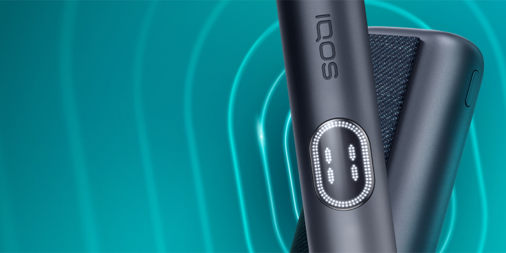 Background image alt: Black IQOS ILUMA i PRIME device and its charger on a dark turquoise background