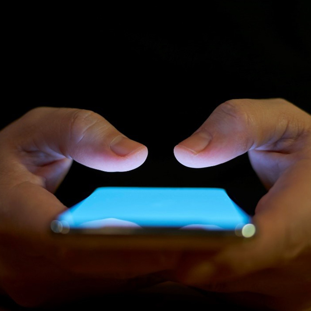 A woman holding an IQOS device looking at a laptop.