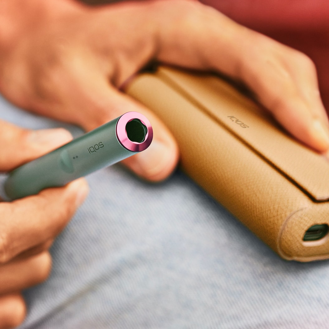 A Jade Green IQOS ILUMA Holder with a ring accessory held by a person with a  leather-like full wrap.