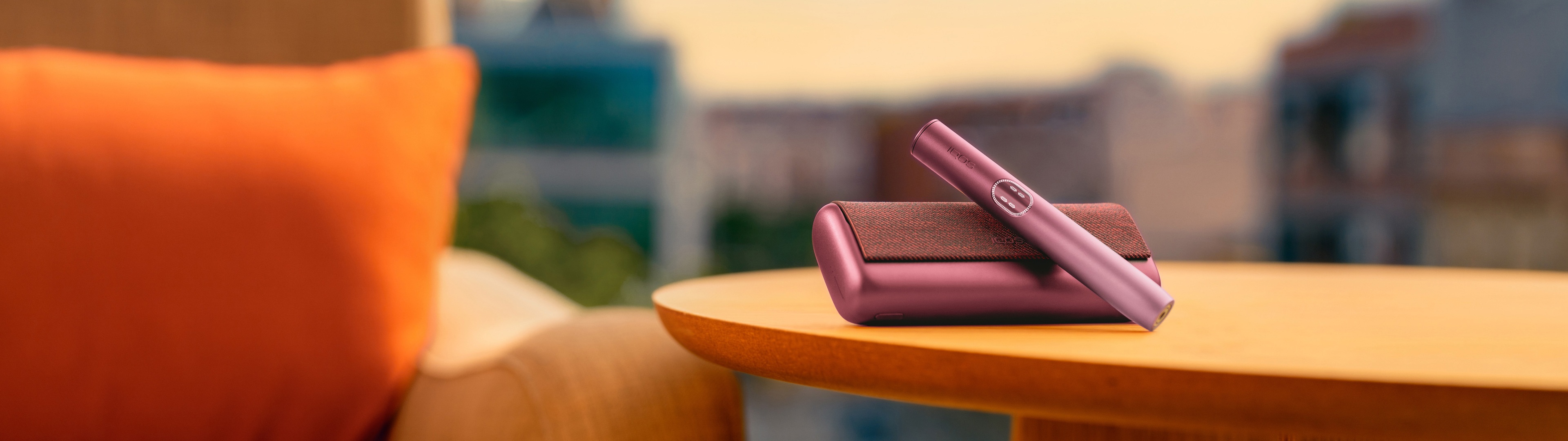 Garnet Red IQOS ILUMA i PRIME device above its charger, on a table near a couch