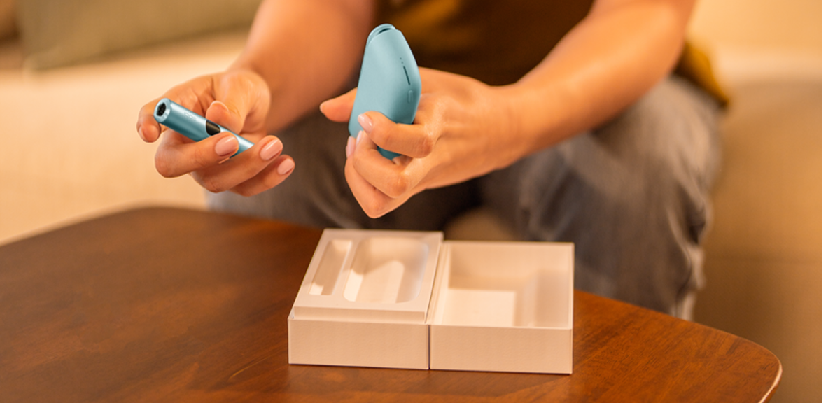 Hands holding an IQOS ILUMA i device in front of a package