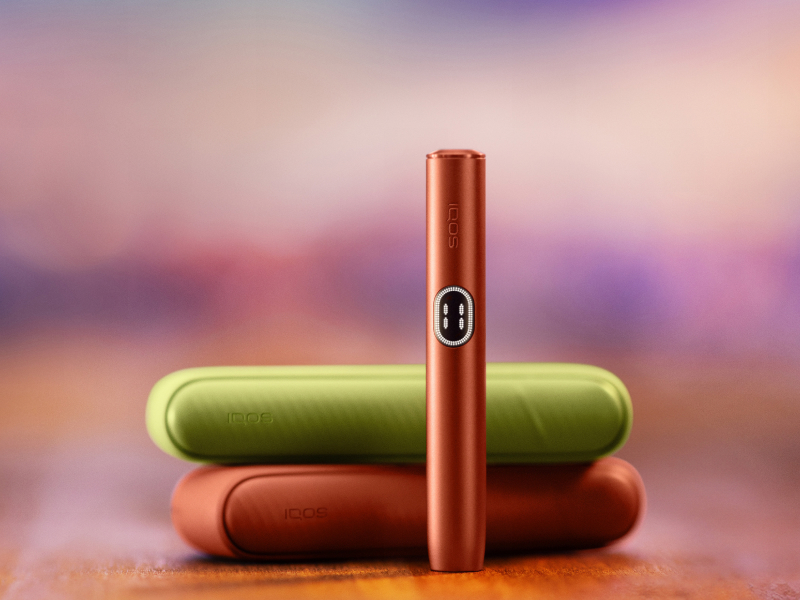 IQOS ILUMA i device standing in front of two chargers of different colours