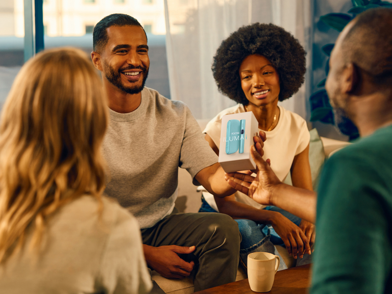 Black IQOS ILUMA i PRIME device and its charger on a light turquoise background