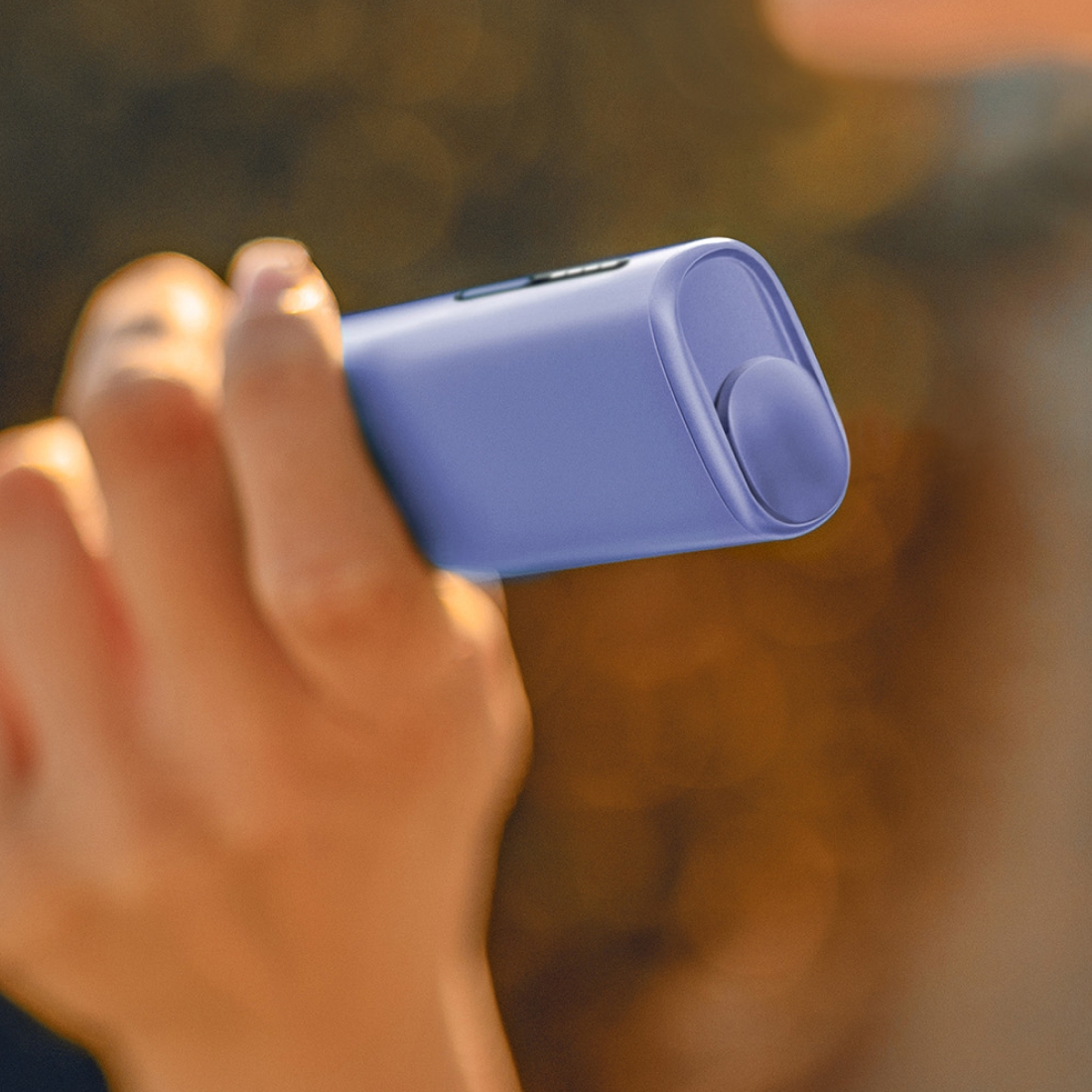 Hand holding a violet IQOS ILUMA i device