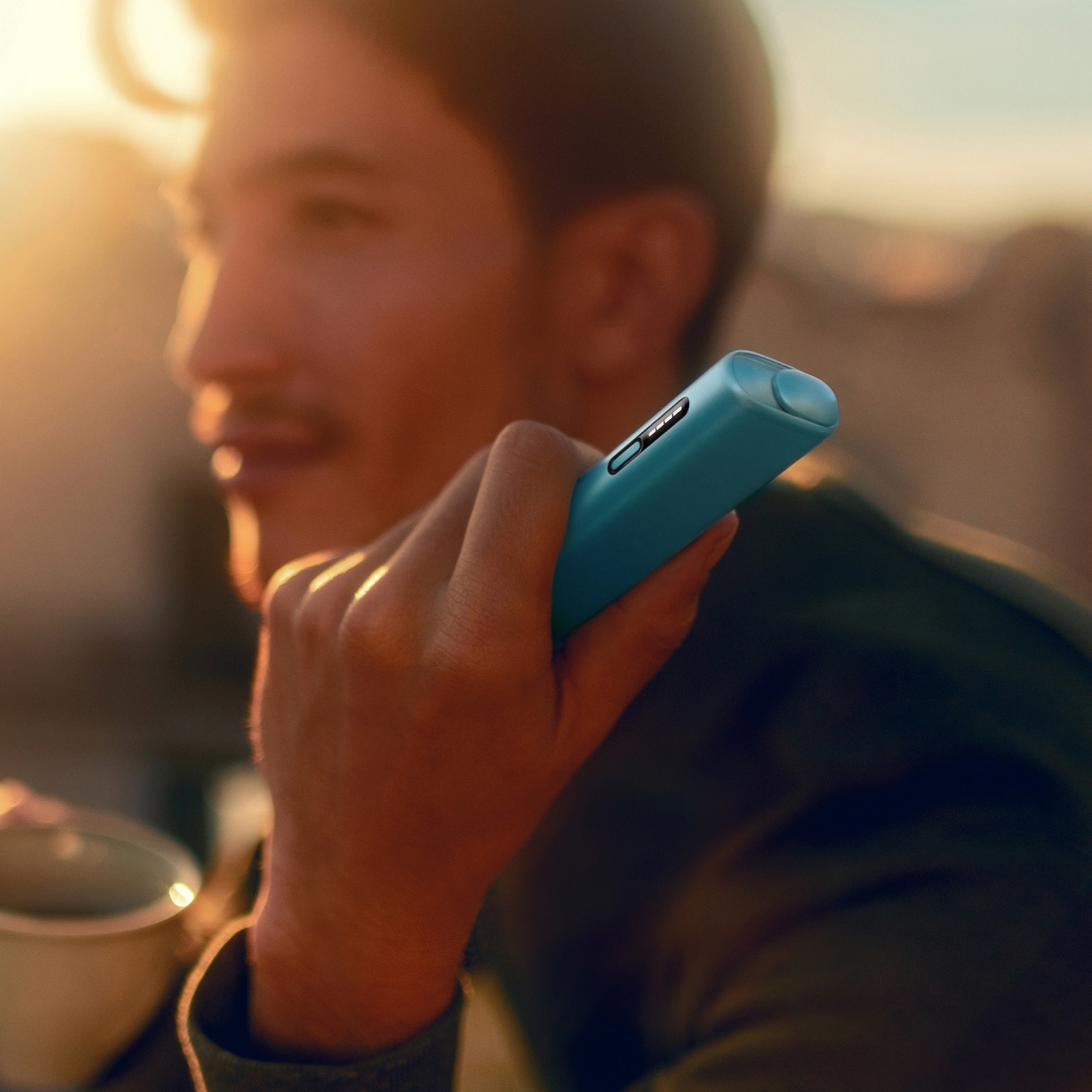 Man holding an IQOS ILUMA i ONE device, sunset background