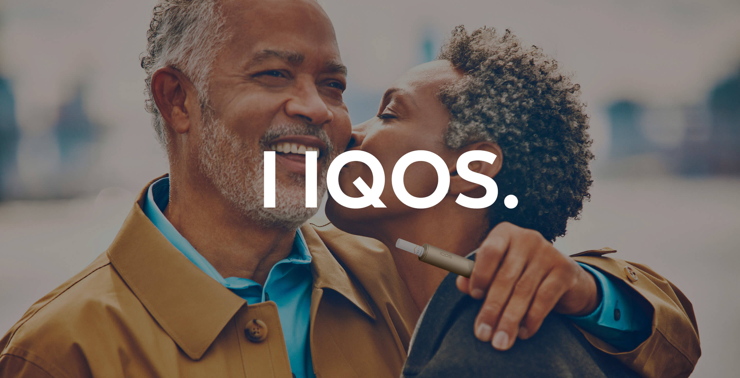 A man holding an IQOS ILUMA device embraces his partner.