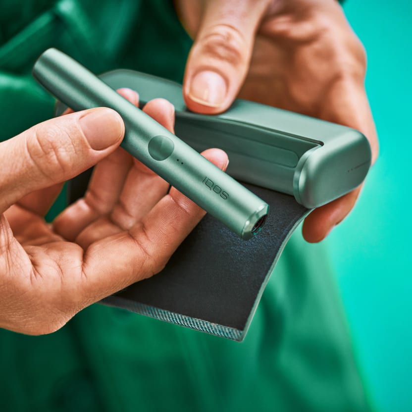 Hands holding a green IQOS device and its charger - green background