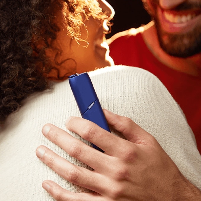 Two people, one holding an IQOS device.