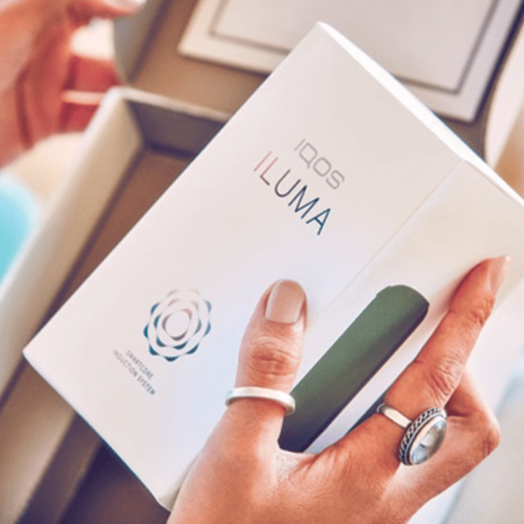 Μία γυναίκα ανοίγει το κουτί μίας IQOS ILUMA συσκευής