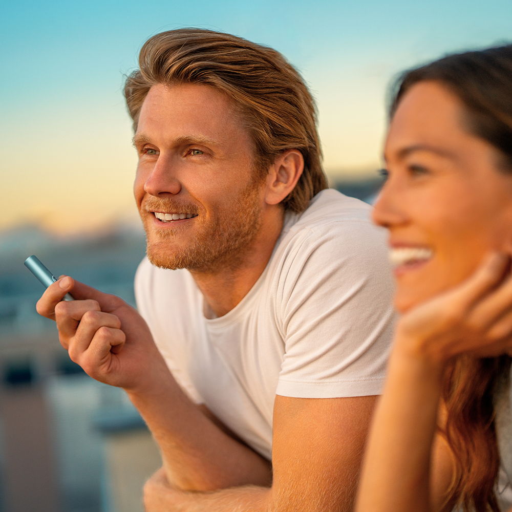 A man holding and IQOS ILUMA and a woman looking at the sunset