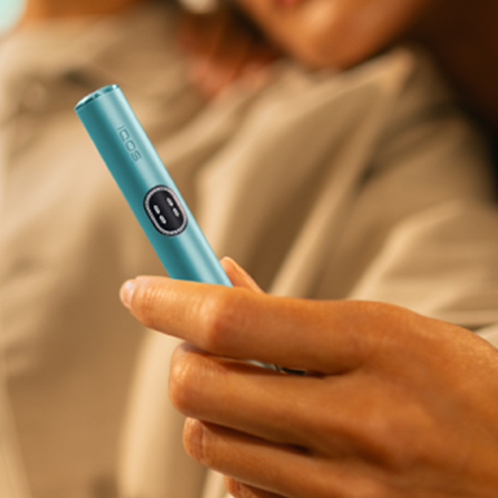 A couple hugging and the woman holds a Breeze Blue IQOS ILUMA i device.