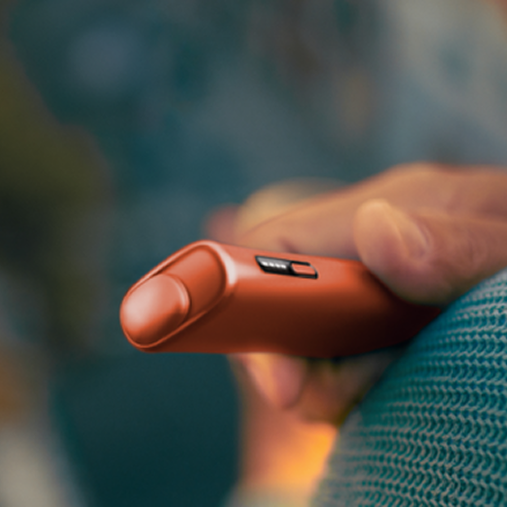 Male hand holding a Terracotta IQOS ILUMA i ONE device.