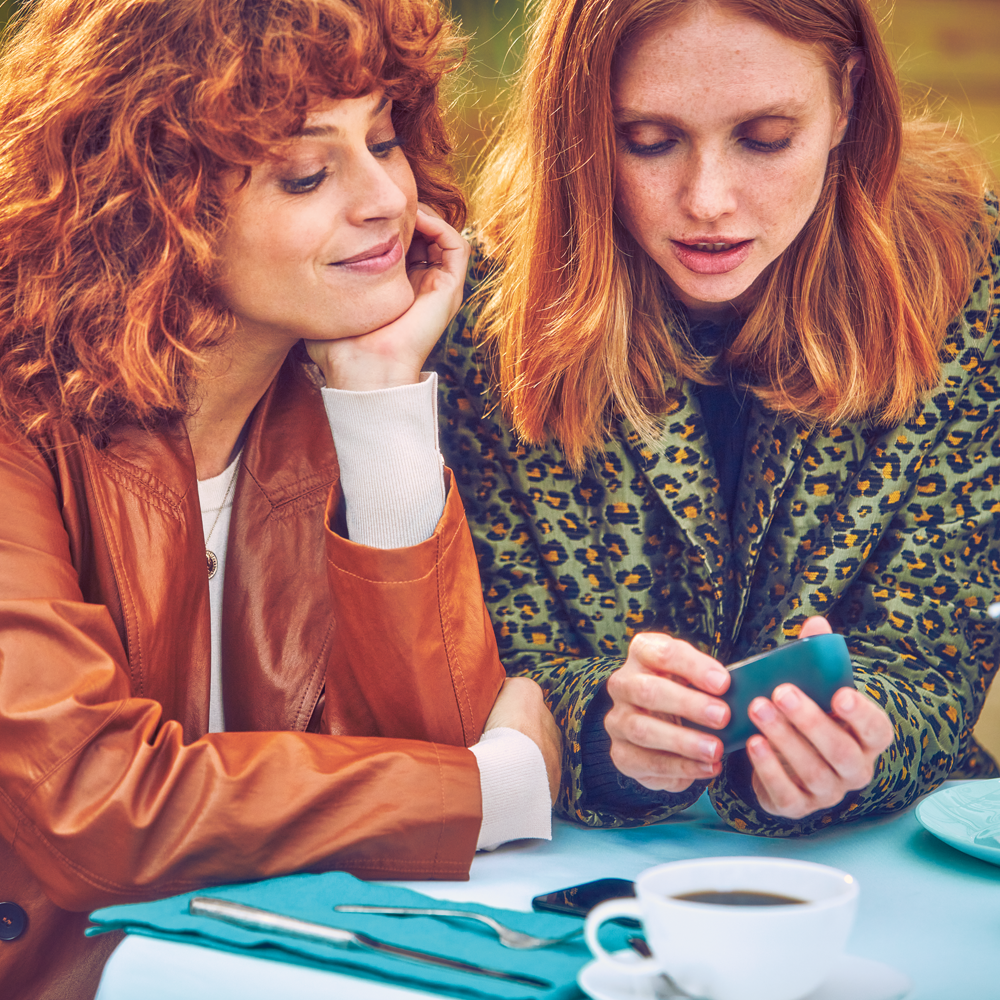 two women with red hair look at an IQOS 3 DUO device