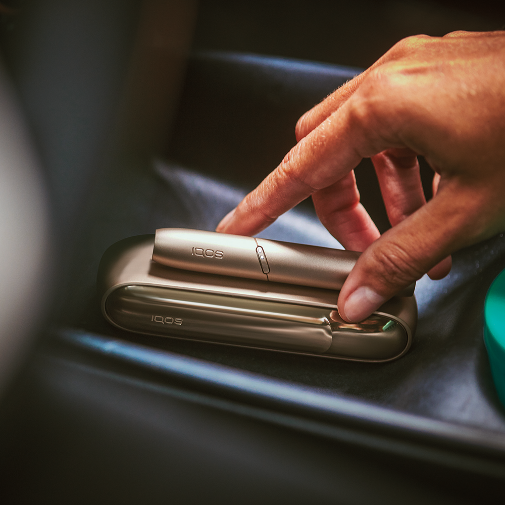 hand placing IQOS 3 DUO Gold on leather surface hand placing IQOS 3 DUO Gold on leather surface