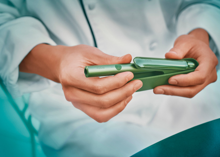 Close up of a hand holding a jade green IQOS ILUMA device.