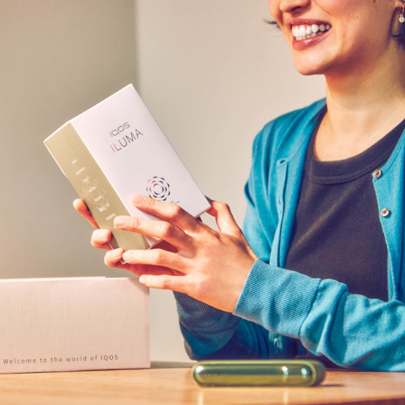 A smiling woman with an IQOS ILUMA device.